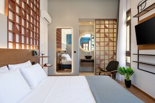 Una habitación de hotel moderna con una cama grande, televisión, planta en maceta y baño visible a través de una puerta de cristal.