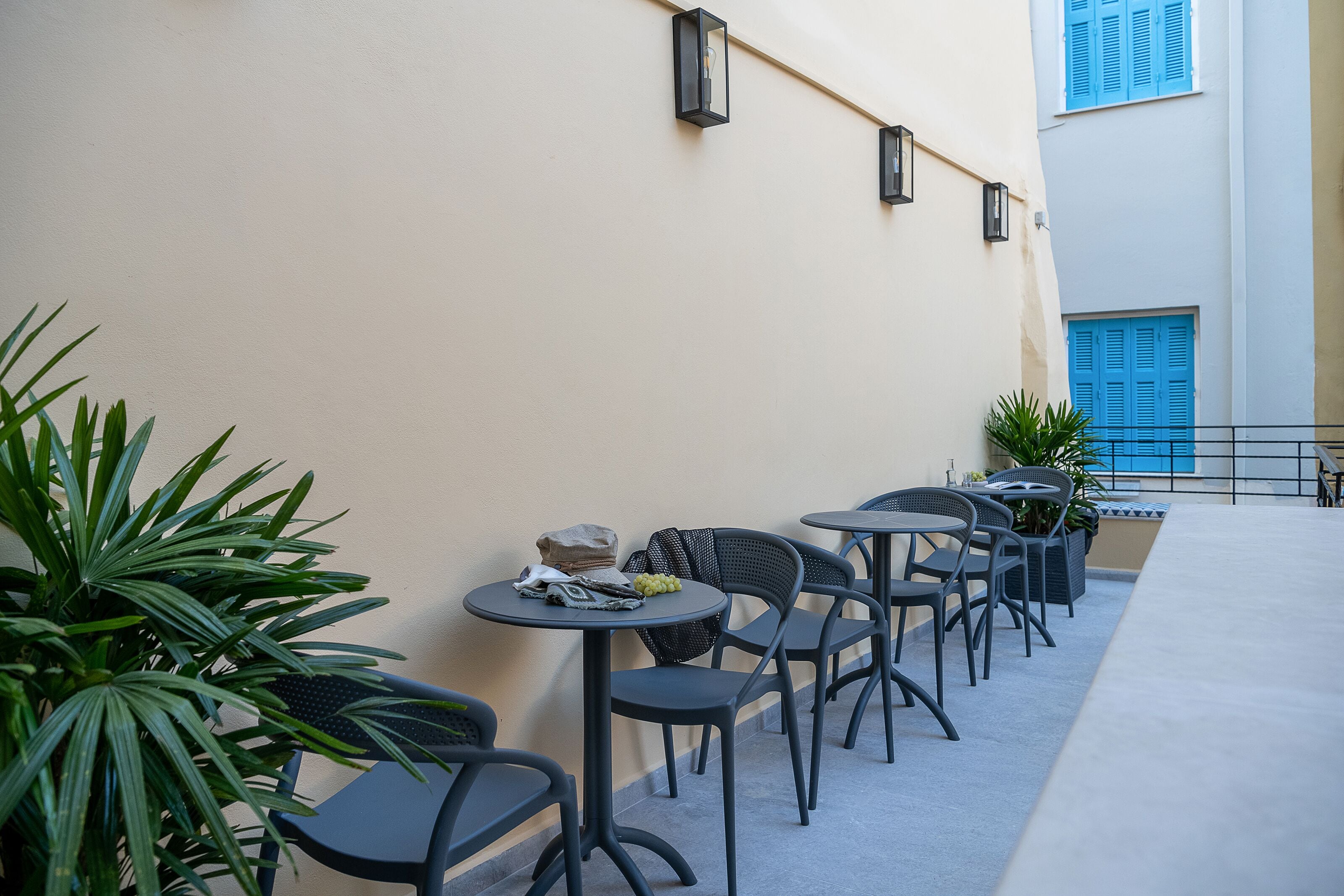 A terrace with outdoor seating, potted plants, and a building with blue shutters.