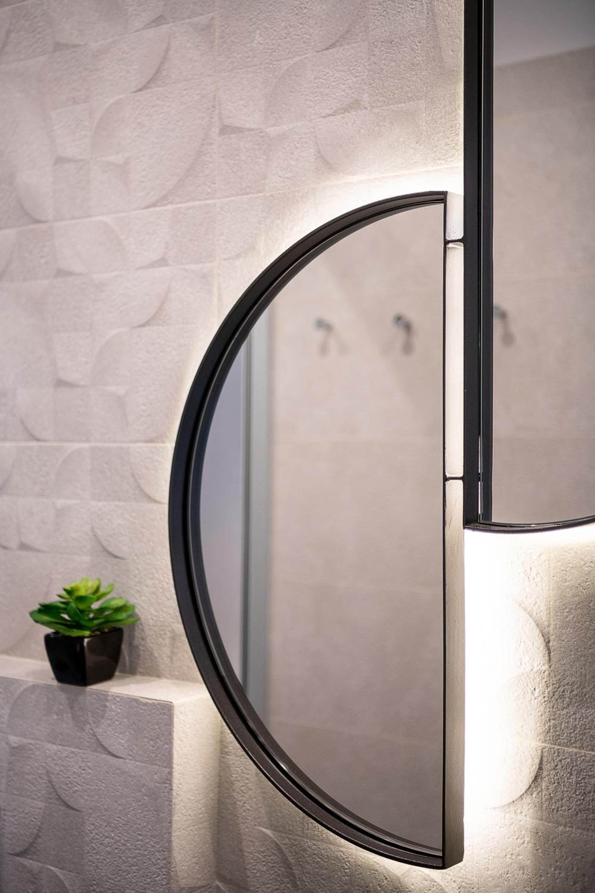 Un baño con un espejo redondo, una pared con textura y una pequeña planta en maceta.