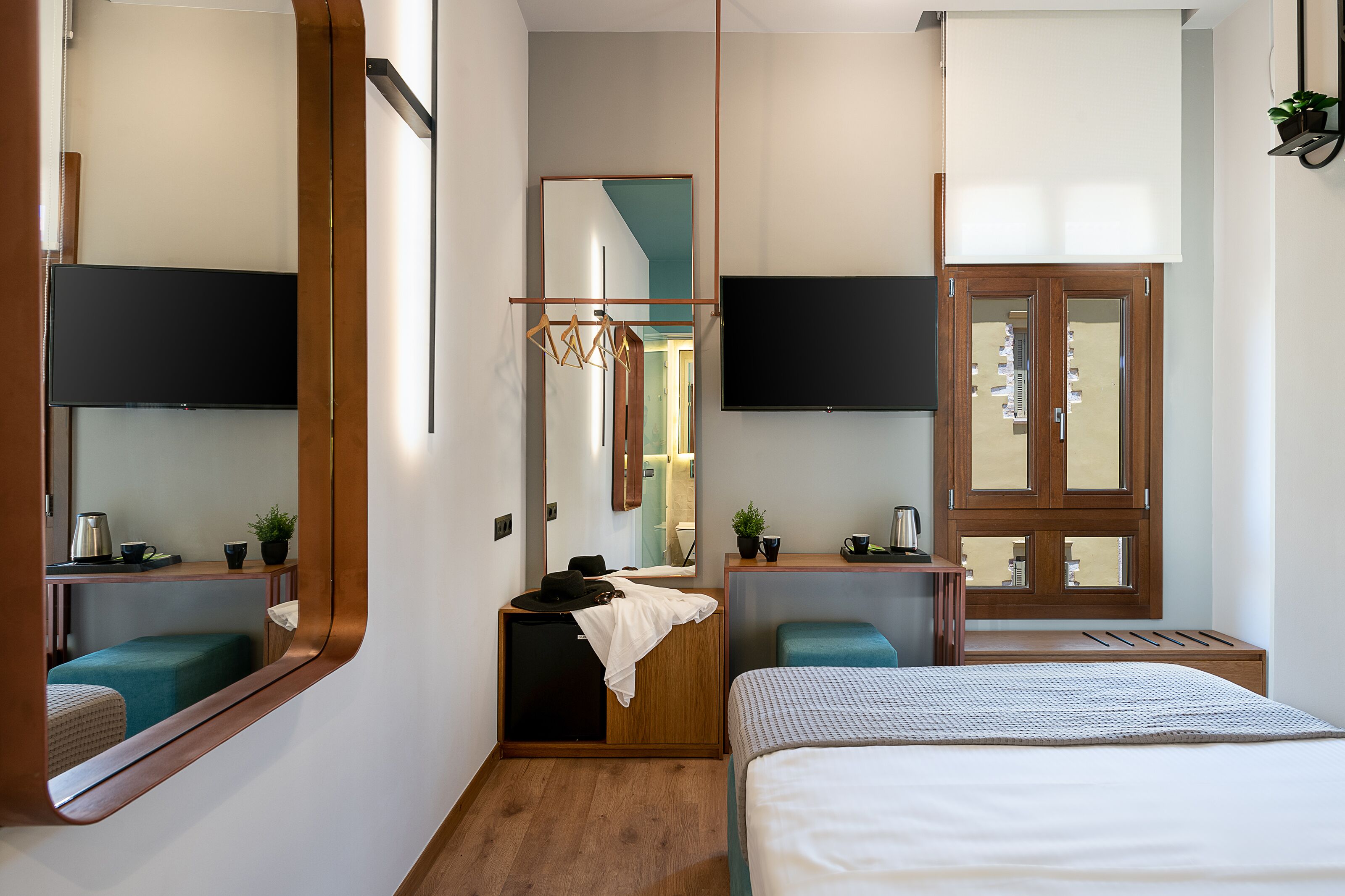 Una habitación de hotel moderna con una cama grande, un escritorio con silla, un pequeño rincón de descanso, un televisor montado en la pared y un espejo amplio.