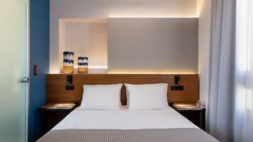 Una habitación de hotel moderna con una cama grande, mesitas de noche, un cabecero de madera y una lámpara fijada a la pared.