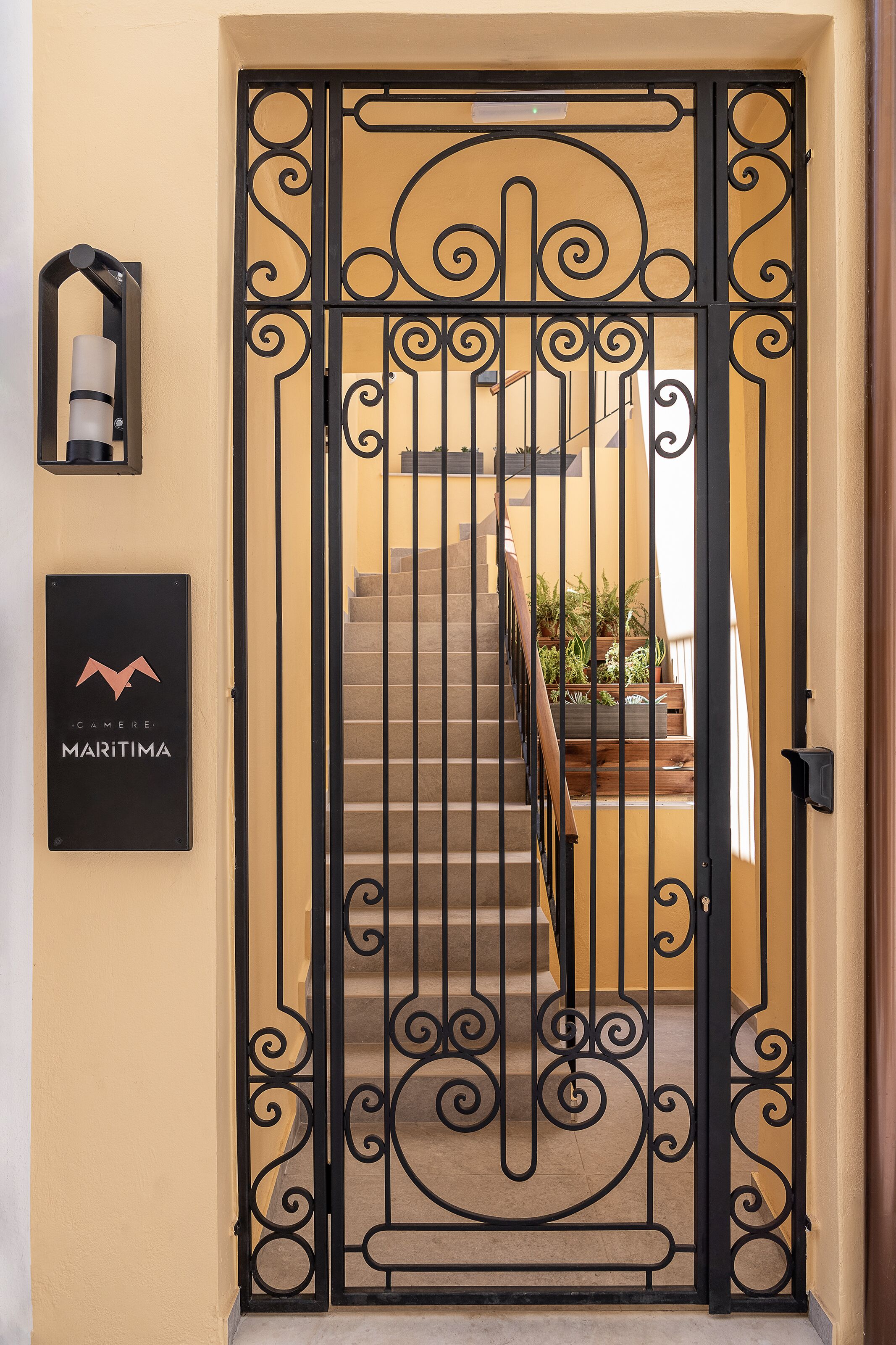Una reja de hierro forjado negro con diseño decorativo, una escalera de madera y un letrero que dice "CAMERE MARITIMA".