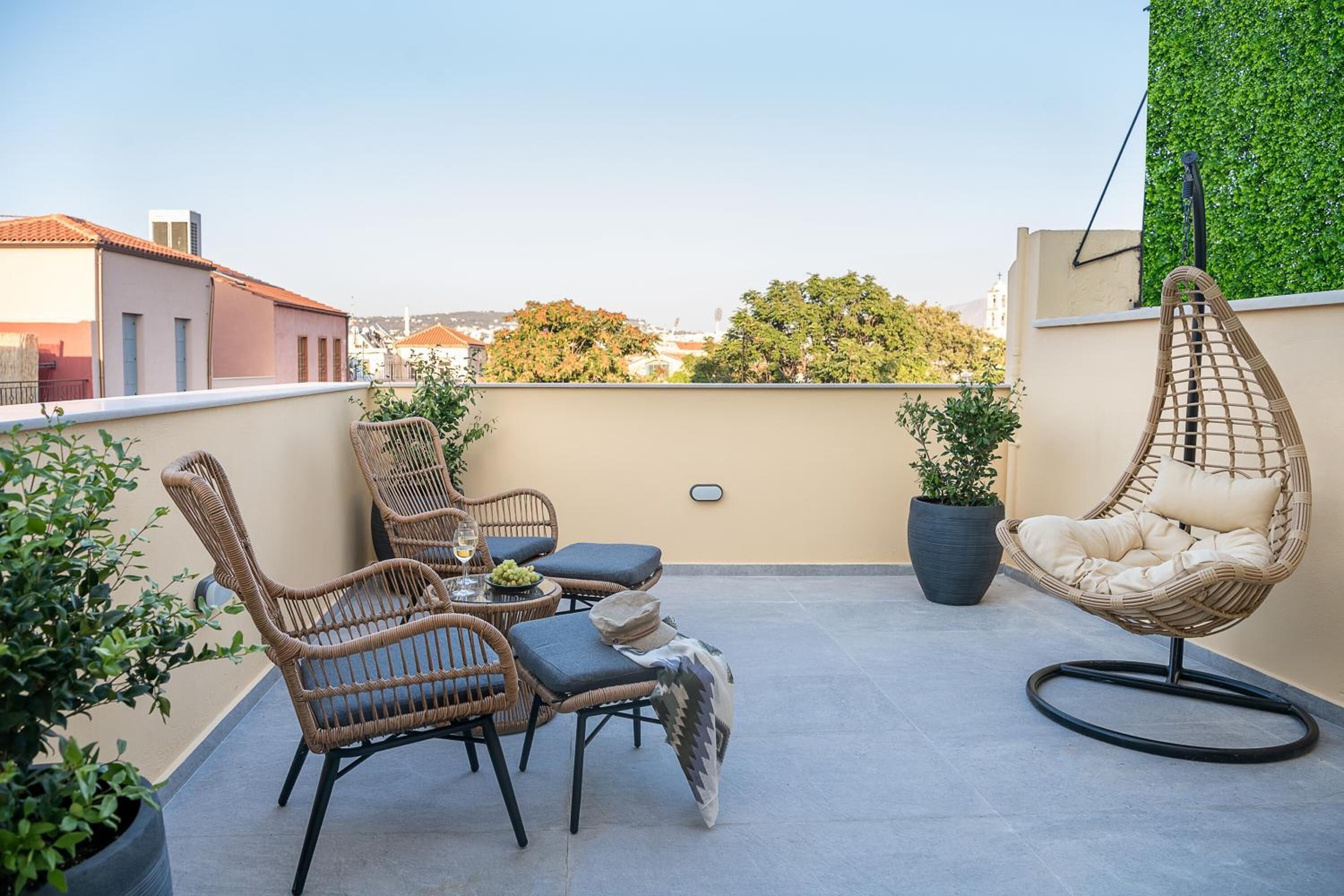 A rooftop terrace with wicker furniture, potted plants, and a hanging chair.