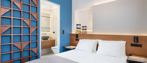 A modern hotel room with a large bed, a wooden headboard, and a blue accent wall.