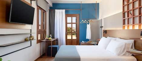 A modern hotel room with a large bed, a flat-screen TV mounted on the wall, a desk with a chair, and a window with curtains.