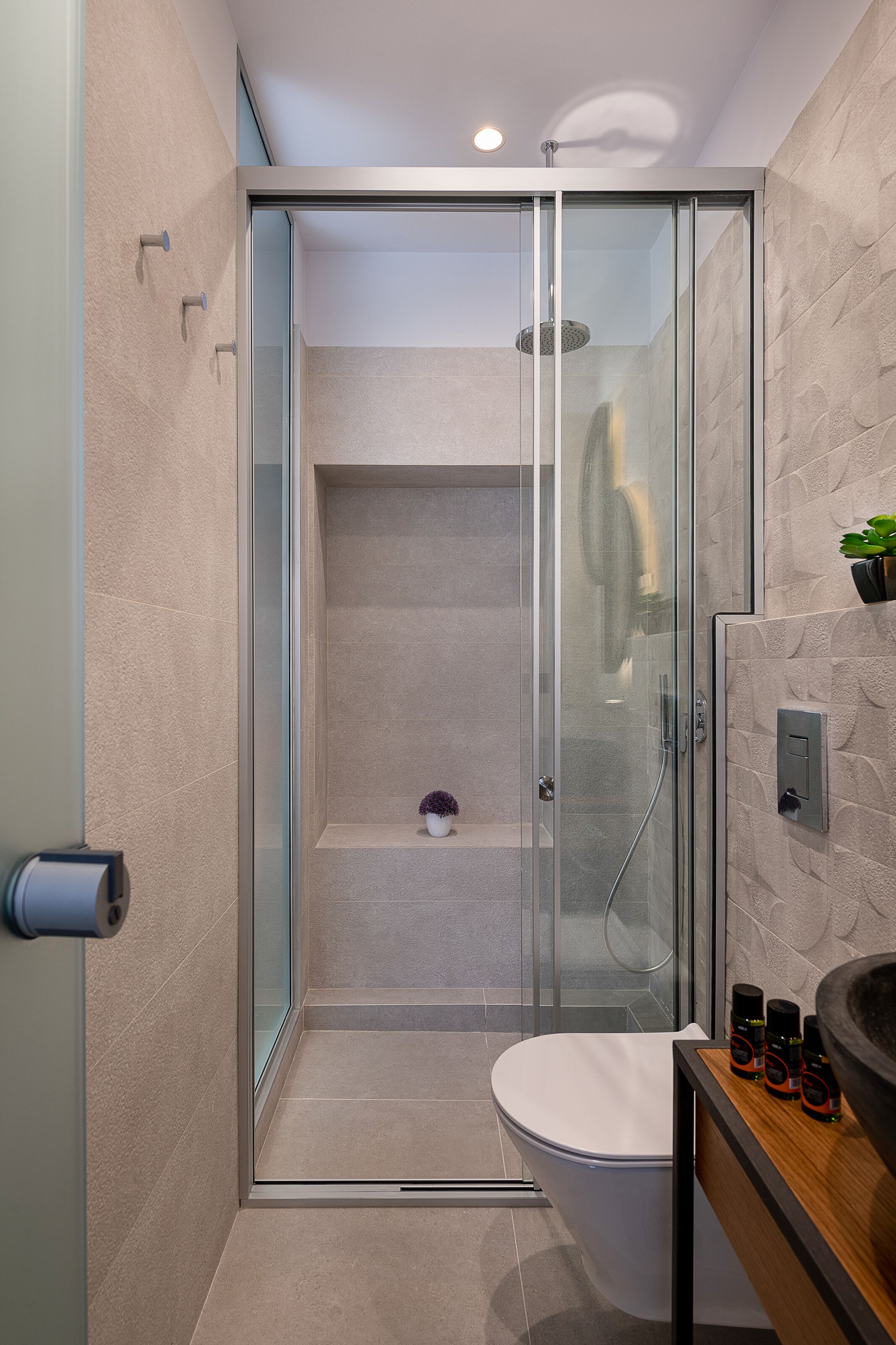 Un baño moderno con ducha envuelta en vidrio, inodoro y lavamanos con artículos de aseo.