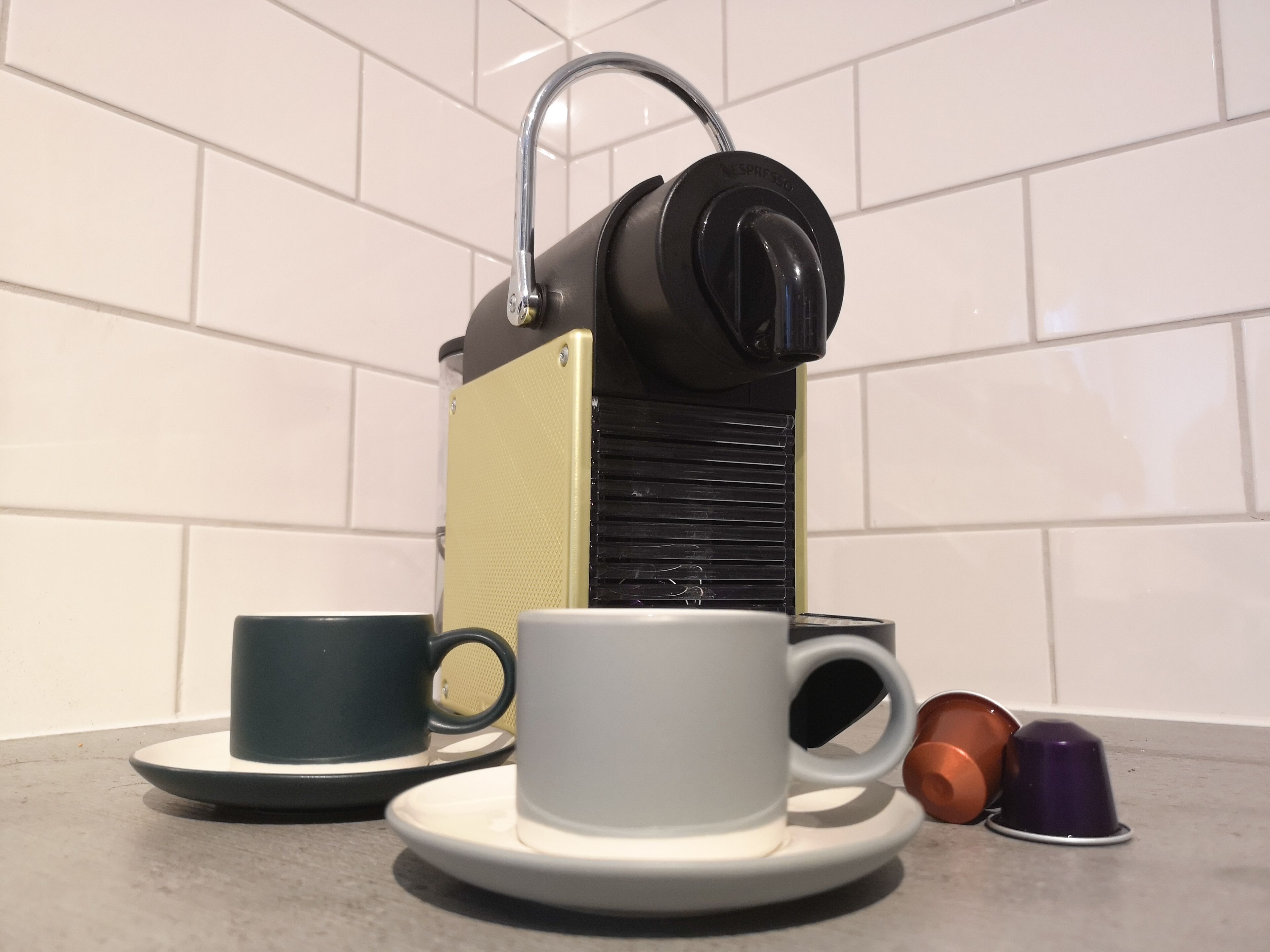 En kaffemaskin med en kopp och ett fat, och två tomma kaffekoppar på en bänkskiva.