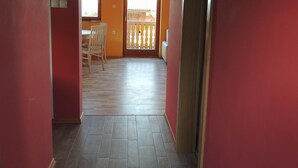 A hallway with red walls, a wooden floor, and a door leading to a balcony with a railing.