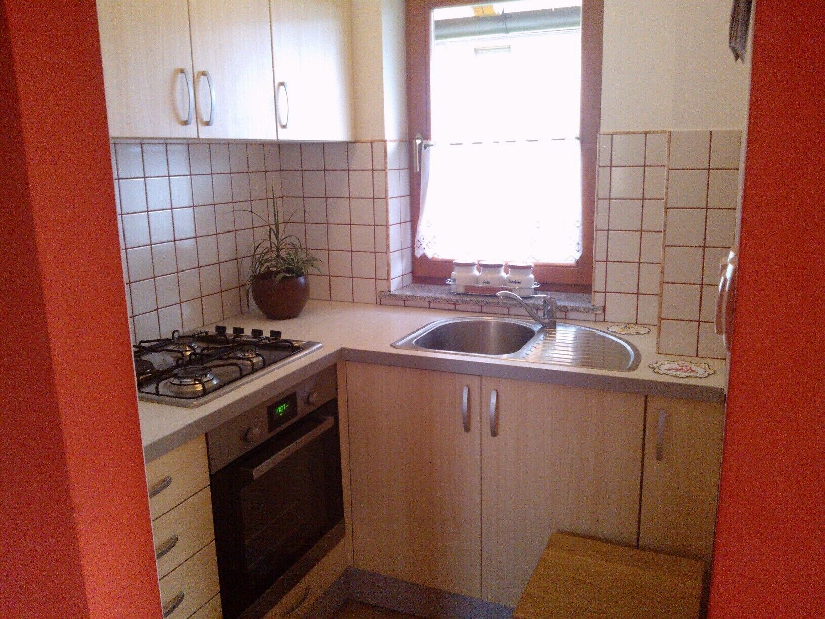 A compact kitchen with white cabinets, a gas stove, a sink, and a window with a view.