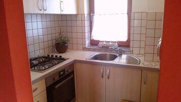 A compact kitchen with white cabinets, a gas stove, a sink, and a window with a view.