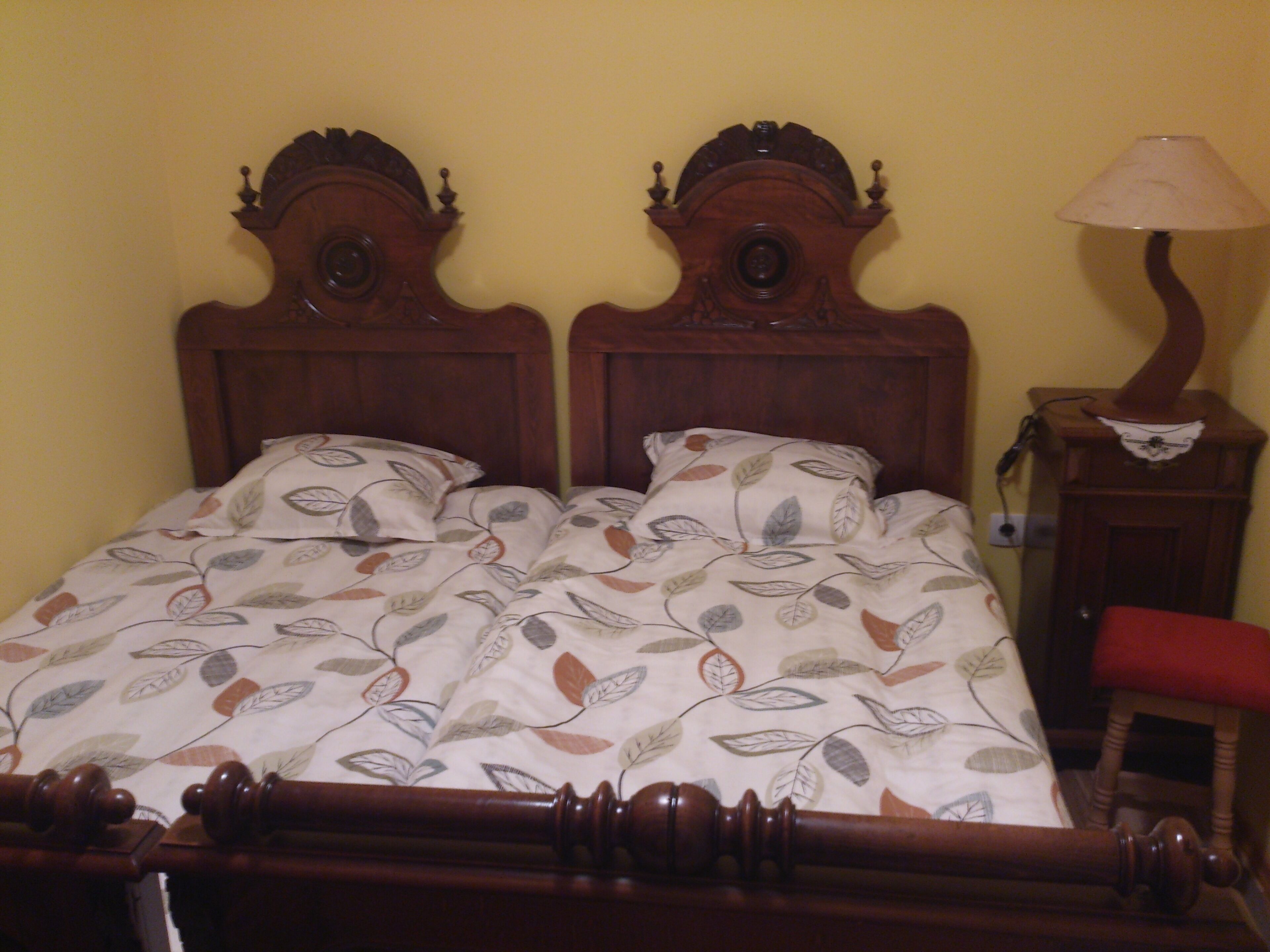 A double bed with a leaf-patterned bedspread, wooden headboard, and a nightstand with a lamp.