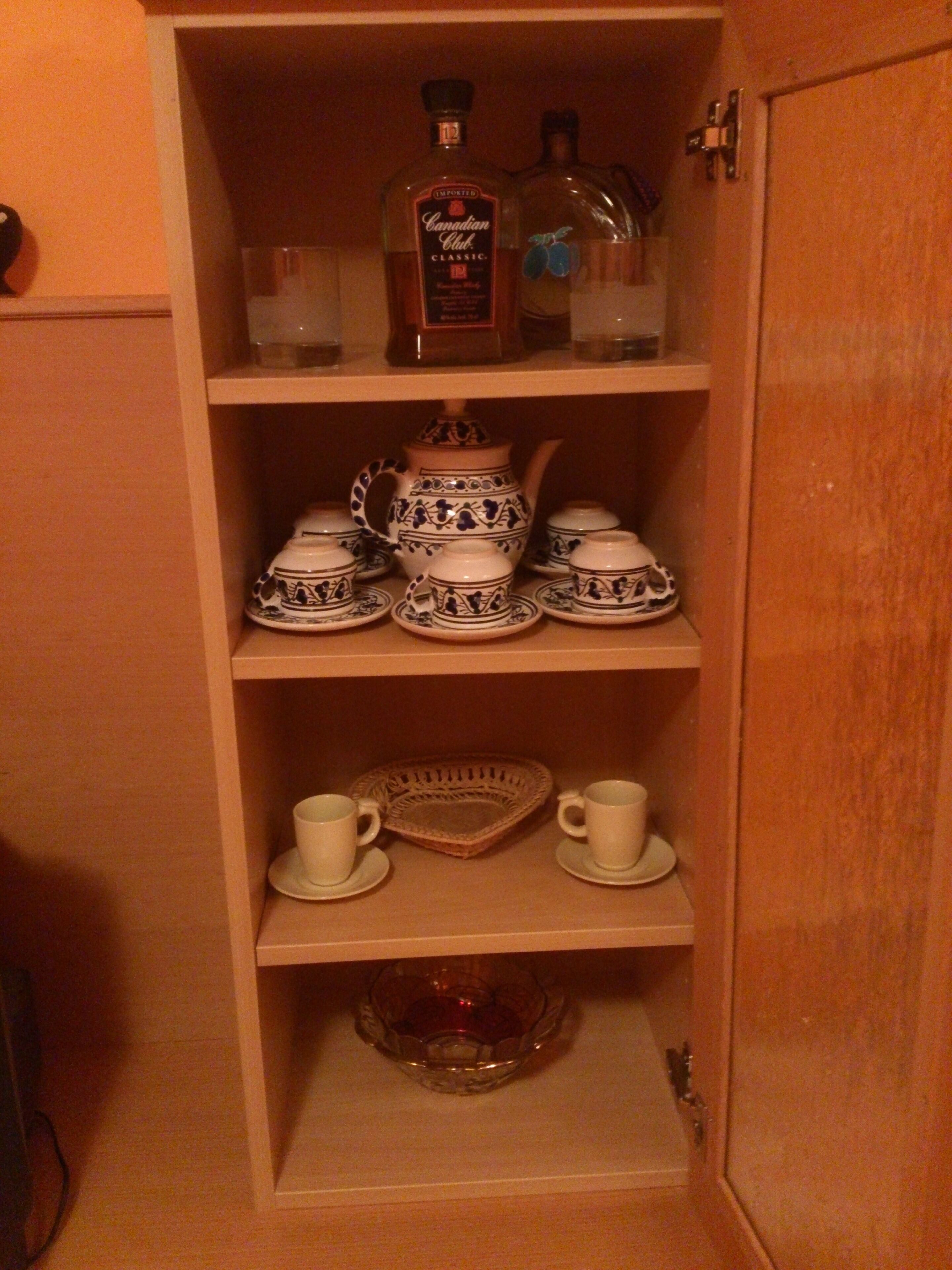 Un mueble de madera con estantes que contienen vajillas de té, tazas y una tetera.