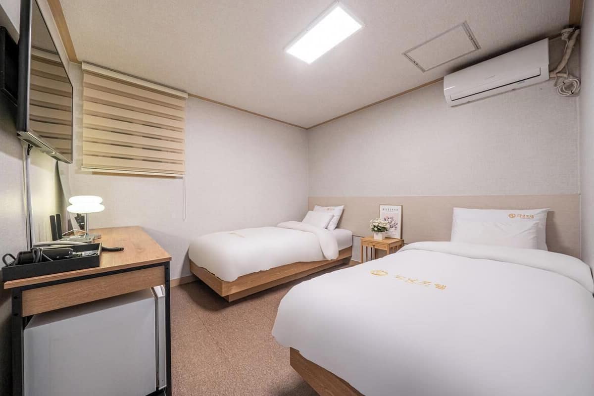 A hotel room with two beds, a desk, a mirror, and an air conditioning unit.