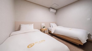 Ein Hotelzimmer mit zwei Betten, einem kleinen Holfnachtkästchen, einer Wandklimaanlage und einer Deckenleuchte.