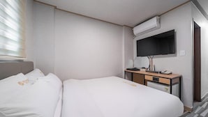 Ein Hotelzimmer mit zwei Betten, einem Schreibtisch, einem Flachbildfernseher, einer kleinen Kommode und einer Klimaanlage.