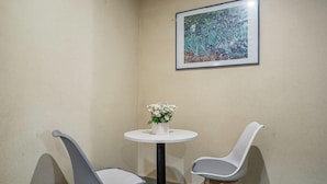 Ein Eckzimmer mit zwei modernen Sesseln, einem kleinen runden Tisch mit Blumenvase und einem gerahmten Pflanzenbild an der Wand.