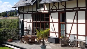 Una casa tradicional amb estructura de fusta i endolls, un balcó, mobles de fusta i plantes en testos.