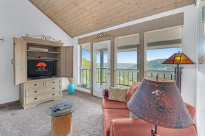 Un salón con televisor, sofá, lámpara y vistas al exterior.