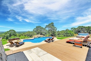 Una terraza de madera con piscina, sillas de descanso y un jacuzzi.
