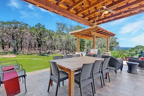 Une terrasse extérieure dotée d’une pergola en bois, d’une table à manger avec des chaises et offrant une vue sur une zone boisée.