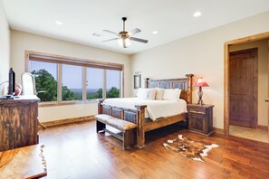 A spacious bedroom with a large window, a wooden bed, a bench, a nightstand, and a ceiling fan. - C L Ranch - Luxury estate with pool, hot tub, and outdoor kitchen! (Fischer)