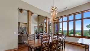 Un comedor amplio con una gran mesa y sillas de madera, una araña y ventanas grandes que ofrecen vistas al exterior.