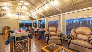 Un comedor con carpas, mesas y sillas de madera, una mesa de centro de vidrio y grandes ventanales con vistas panorámicas.