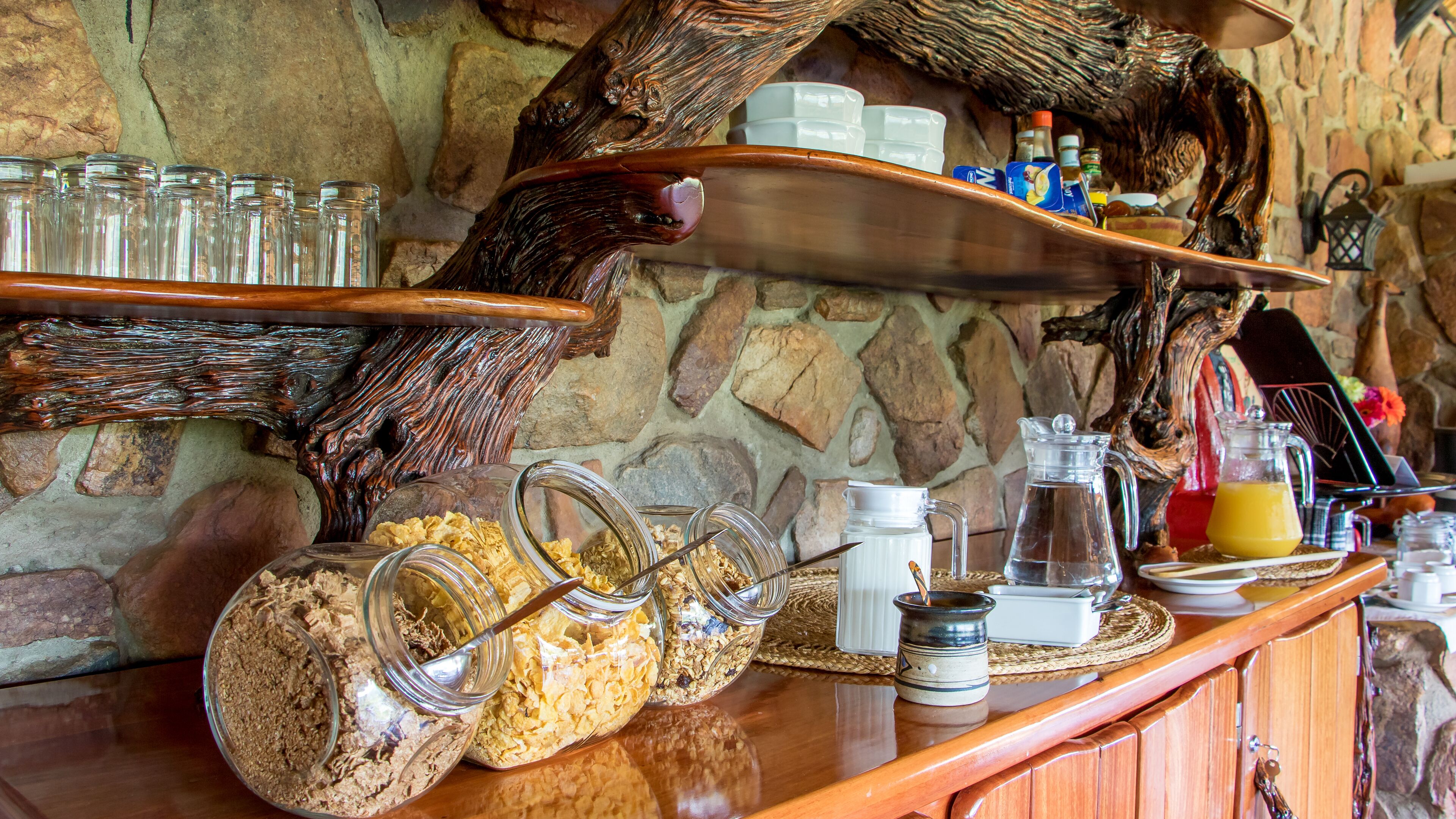 Un rústico espacio de bar con estantes de madera, frascos de comida y un fondo de pared de piedra.