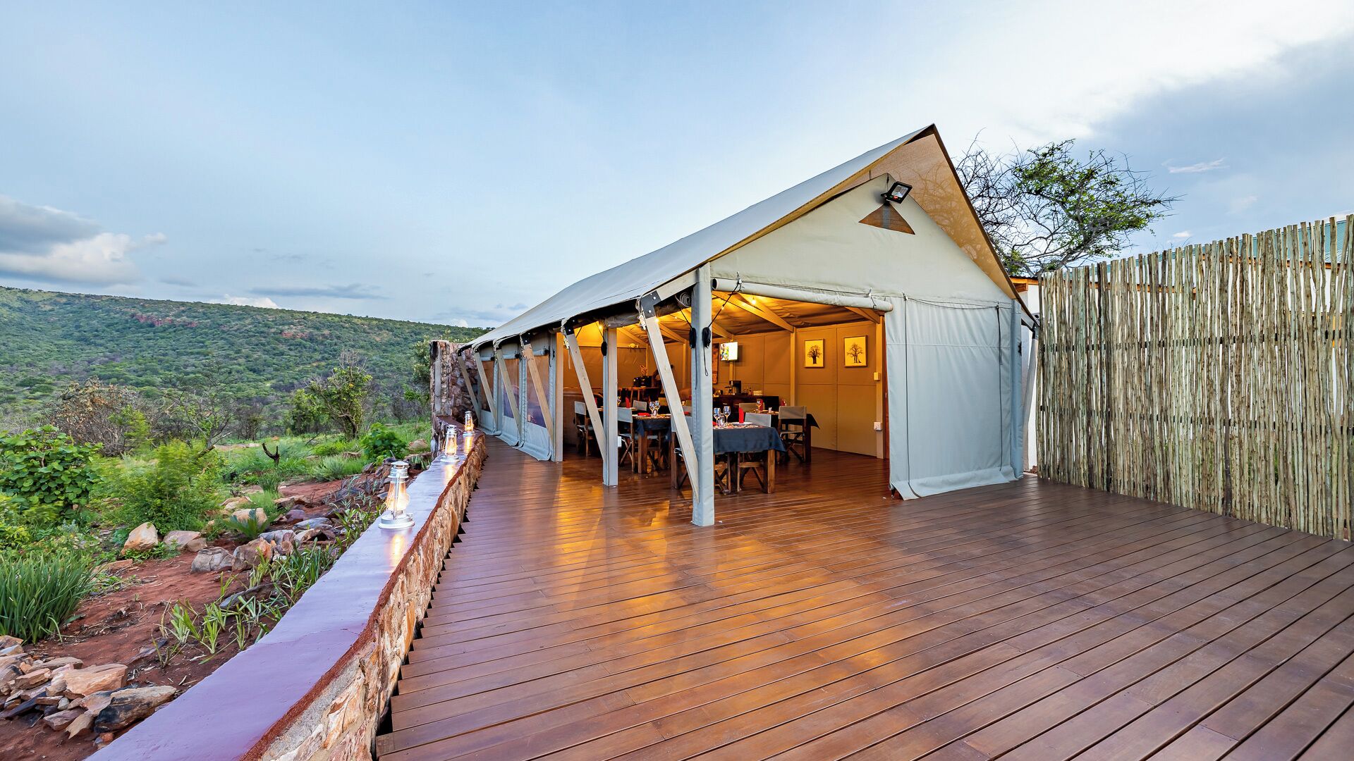 A tented accommodation with a wooden deck, dining area, and a view of the surrounding landscape.