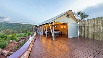 A tented accommodation with a wooden deck, dining area, and a view of the surrounding landscape.
