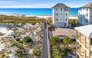 Un hotel frente al mar con vista a la playa, un paseo marítimo empedrado y una estructura tipo torre.