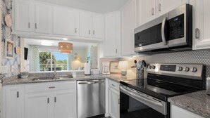 A modern kitchen with white cabinetry, stainless steel appliances, and a view to the outside.