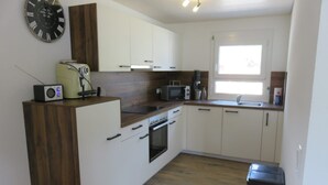 Una cocina moderna con armarios blancos, un panel de acento de madera, horno empotrado, microondas y un reloj en la pared.
