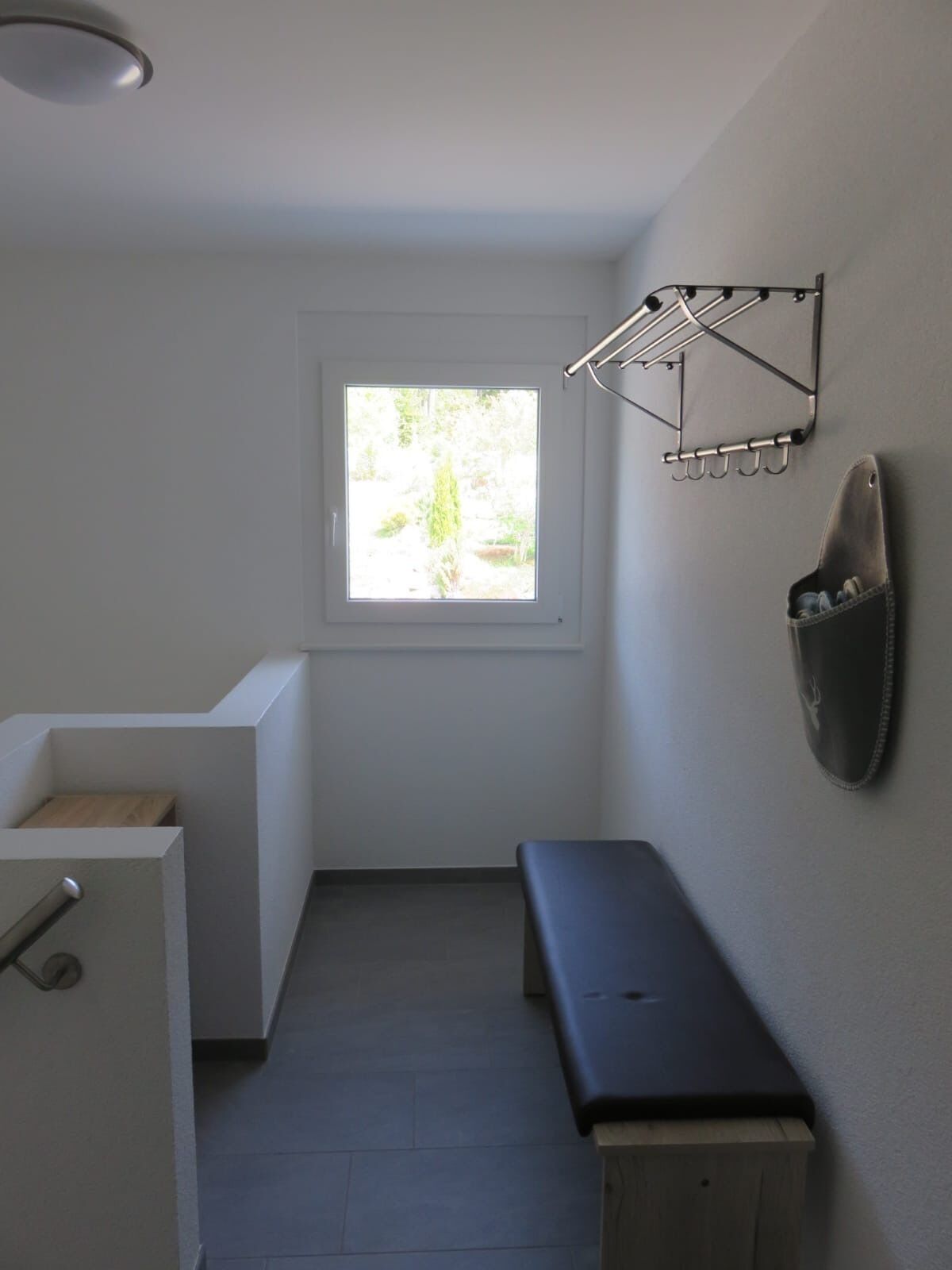 A small, clean bathroom with a window, a towel rack, and a bench.