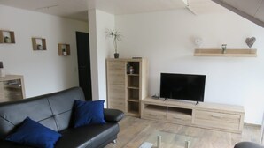Una sala de estar moderna con un sofá de cuero negro, una mesa de centro de vidrio y un mueble de televisión de madera.