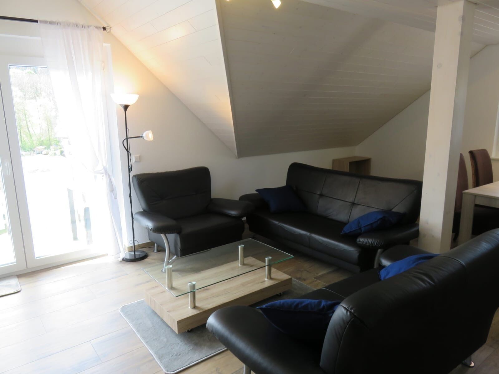 Ein modernes Wohnzimmer mit einem Glastisch, zwei schwarzen Ledersofas und einer Stehlampe.