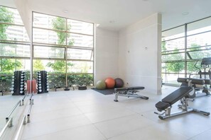 A gym with exercise equipment, large windows, and a view of buildings and trees. - Wynwood Studio - Pool, Gym, Mall & Wifi (Vitacura)
