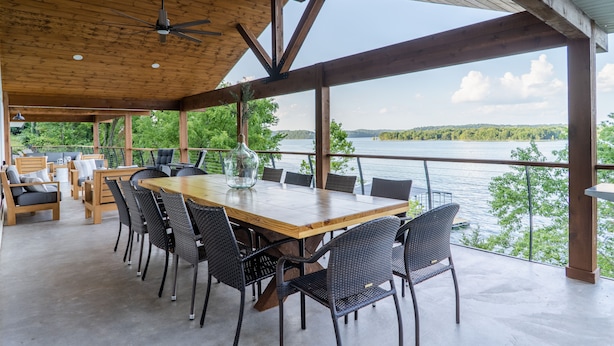 Un vaste espace extérieur aménagé pour les repas, avec une table et des chaises en bois, donnant sur un lac.