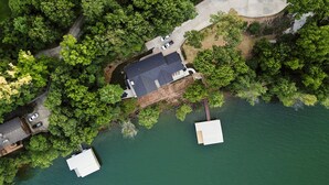 Vue aérienne d’une propriété au bord du lac, avec un quai, une aire de stationnement et un bâtiment doté d’un toit foncé.