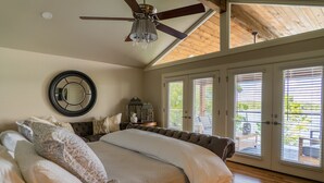 Une chambre spacieuse avec un grand lit, un ventilateur de plafond et une vue sur l’extérieur grâce à de grandes portes-fenêtres coulissantes.