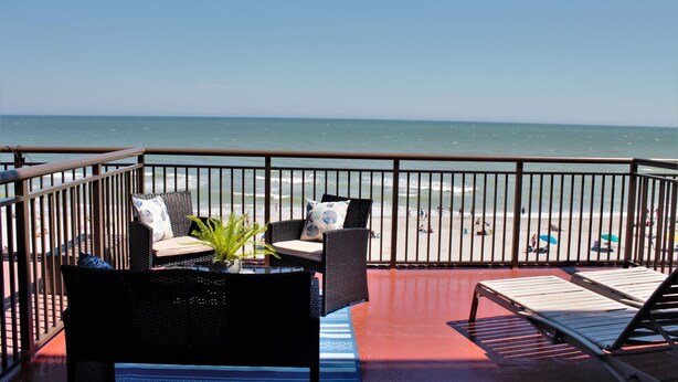 A balcony with wicker furniture, a potted plant, and a view of the beach. - Gorgeous View Oceanfront Condo w/ Hug Sundeck Balcony (Myrtle Beach)
