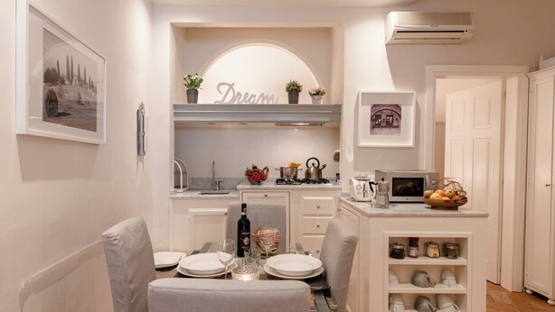 Une cuisine compacte avec des meubles blancs, un coin repas avec une table pour deux personnes et un petit îlot central doté de rangements.