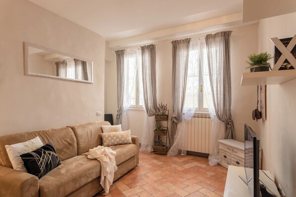 Una sala de estar con un sofá color beige, un espejo, un radiador y un mueble para televisor.