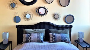 A bedroom with a bed, two nightstands, and various wall decorations including mirrors and sunburst patterns.