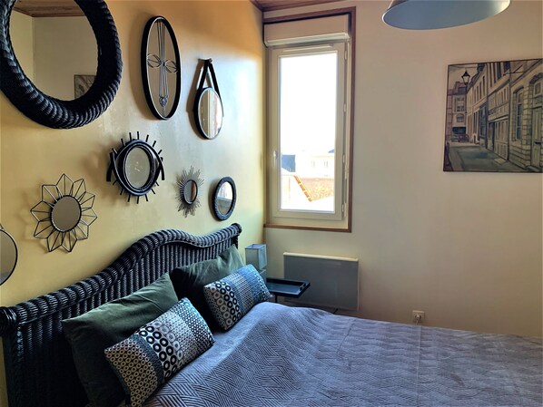 A bedroom with a bed, multiple wall mirrors, and a window with a view of buildings.
