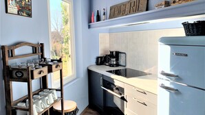 A kitchen with a vintage refrigerator, a coffee maker, and a wooden rack with cups.