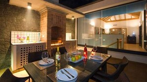 Un espace de restauration en plein air doté d’une cheminée en briques, d’une cloison en verre et d’une table dressée pour deux personnes.
