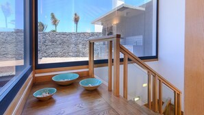 Un intérieur moderne avec un escalier en bois, un mur en pierre et une vue sur les palmiers et les bâtiments à l’extérieur.