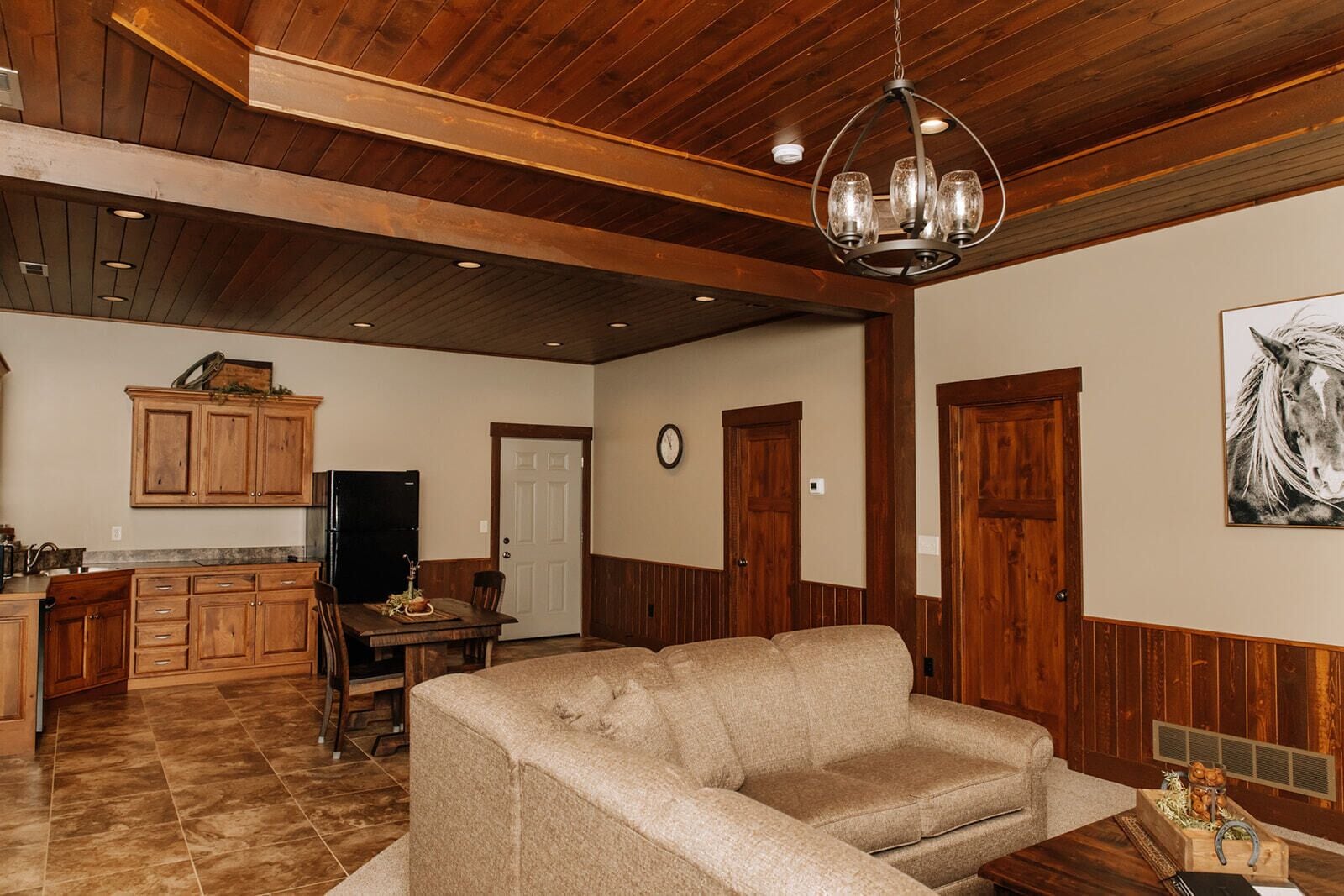 Uma sala de estar ampla com teto de madeira, uma mesa de jantar com cadeiras, um sofá e uma área de cozinha com armários de madeira e uma geladeira.