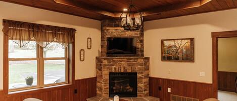 A cozy living room with a stone fireplace, wooden ceiling, and comfortable seating.